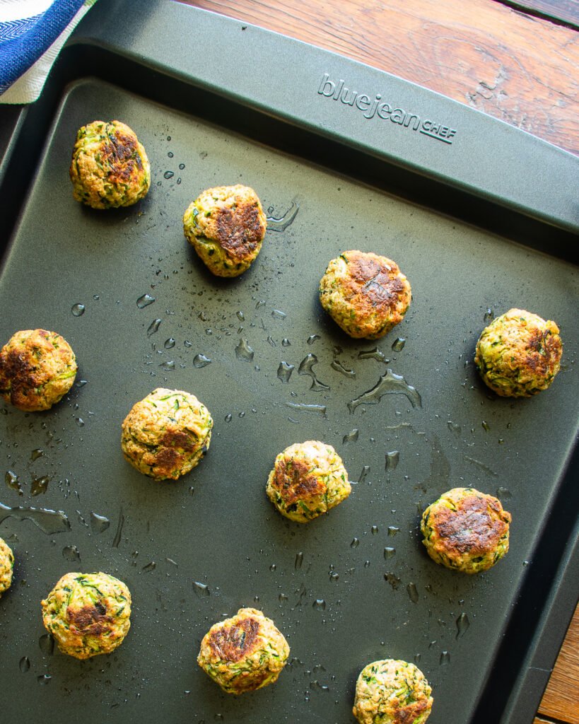Cooked zucchini meatballs on a sheet pan.