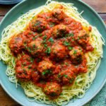 A large green platter with spaghetti and zucchini meatballs in marinara with parsley on top