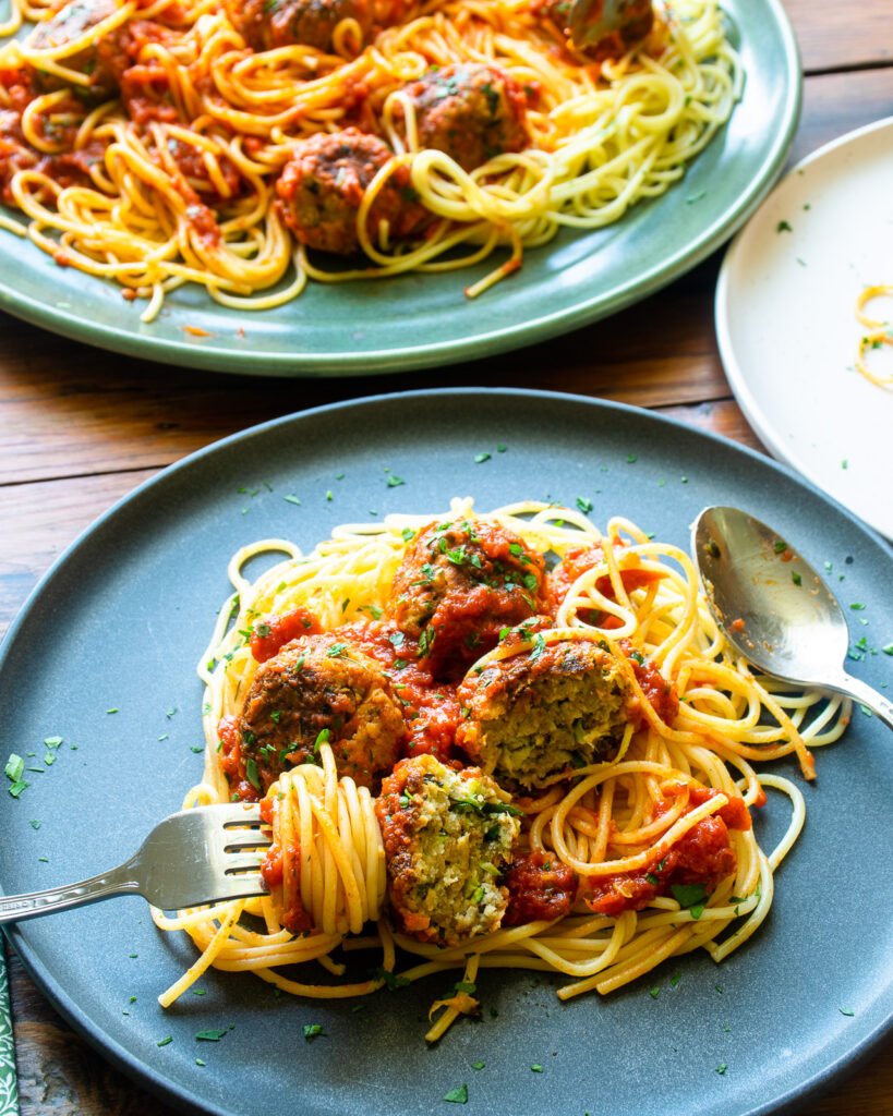 Zucchini Meatballs on spaghettini on a grey plate with more in the background.