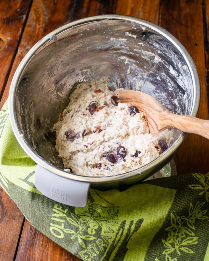 No knead bread dough mixed together in a stainless steel bowl with a wooden spoon.