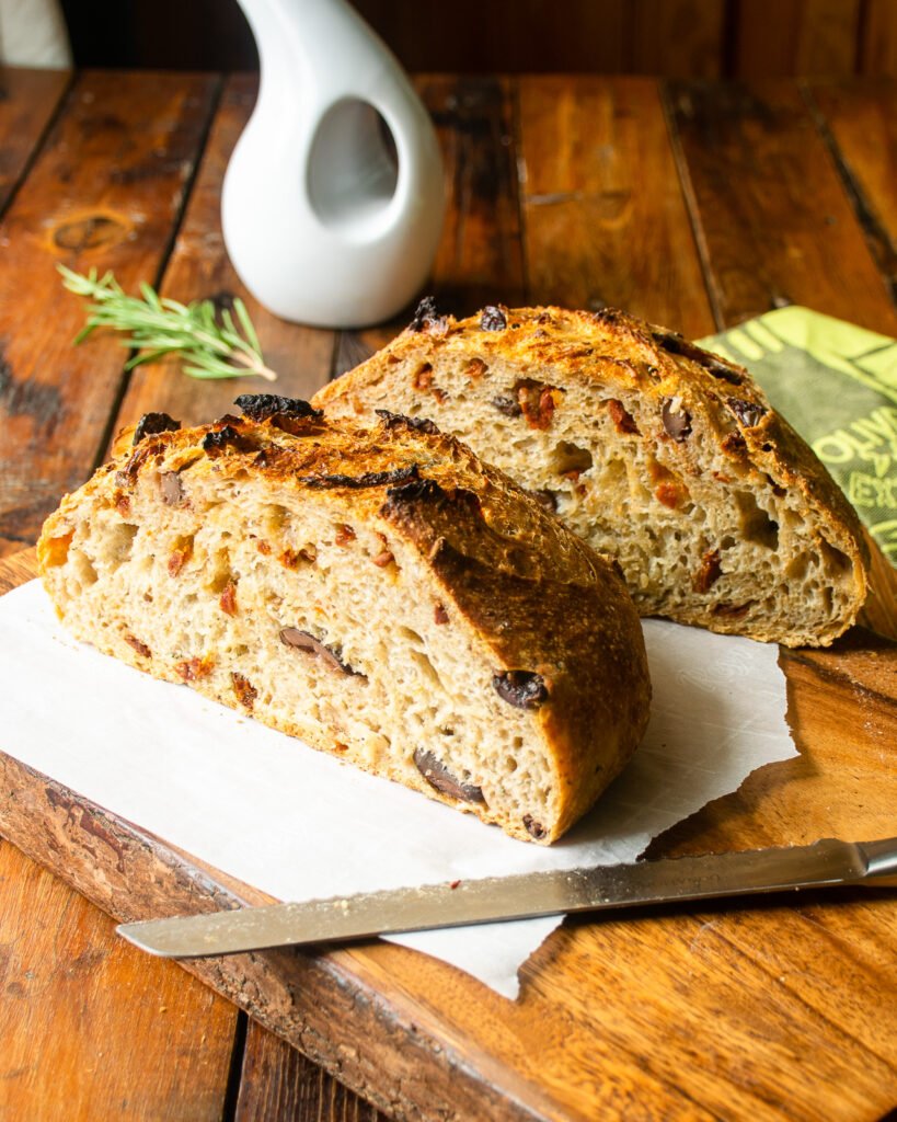 Sun-dried tomato no knead bread, cut in half on a cutting board with a bread knife.