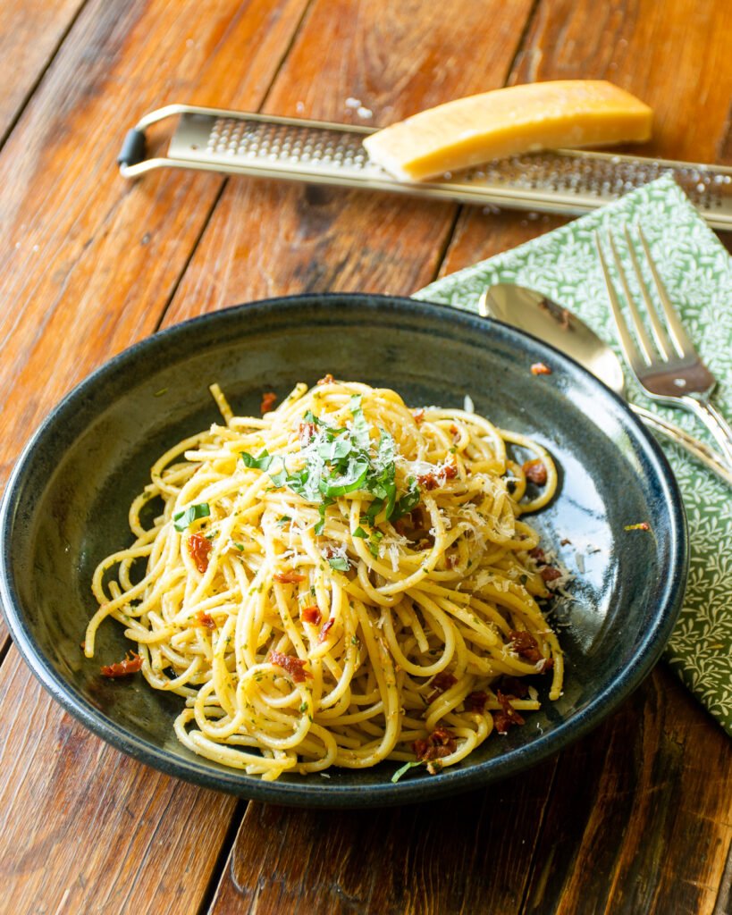 Sun-dried tomato pesto pasta in a black bowl on a wooden table.