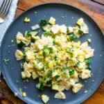 Farfalle with Zucchini, Corn and mascarpone cheese on a black plate on a wooden table.
