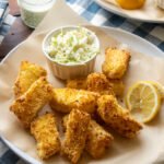 Air fryer fish sticks on a parchment lined plate with coleslaw and a lemon wedge.