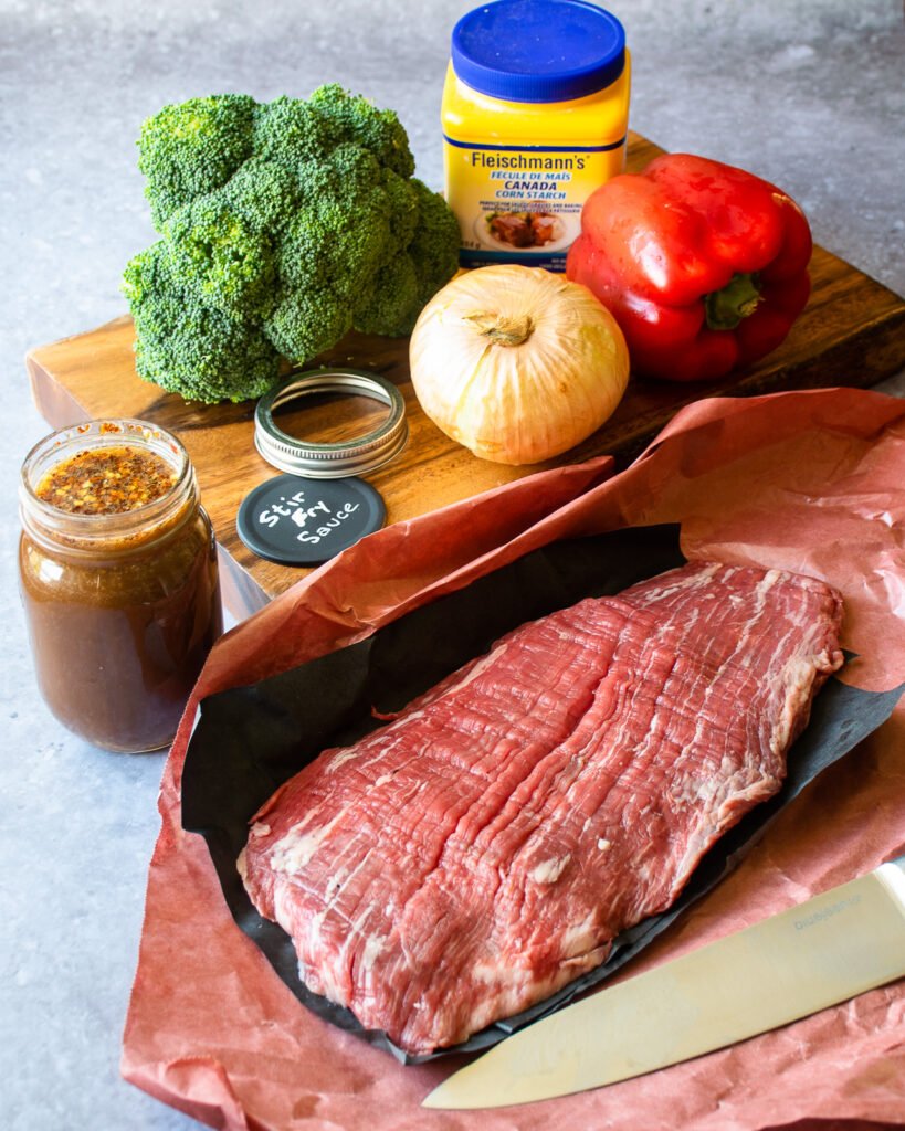 Ingredients on a counter - flank steak, red pepper, onion, broccoli, cornstarch and stir fry sauce.