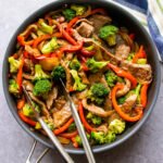 Beef and Broccoli Stir Fry in a large skillet with tongs and a blue and white striped towel.