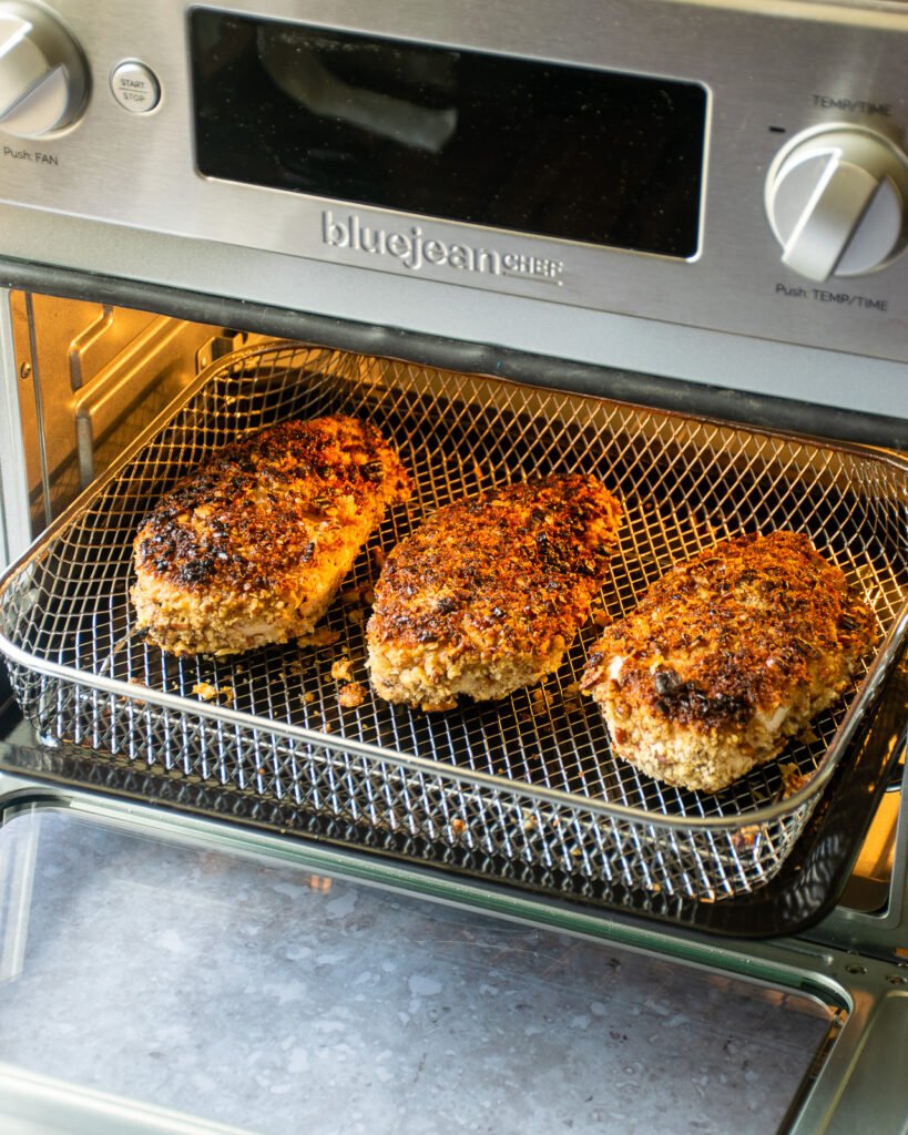 Pecan crusted chicken breasts cooking in an air fryer oven.
