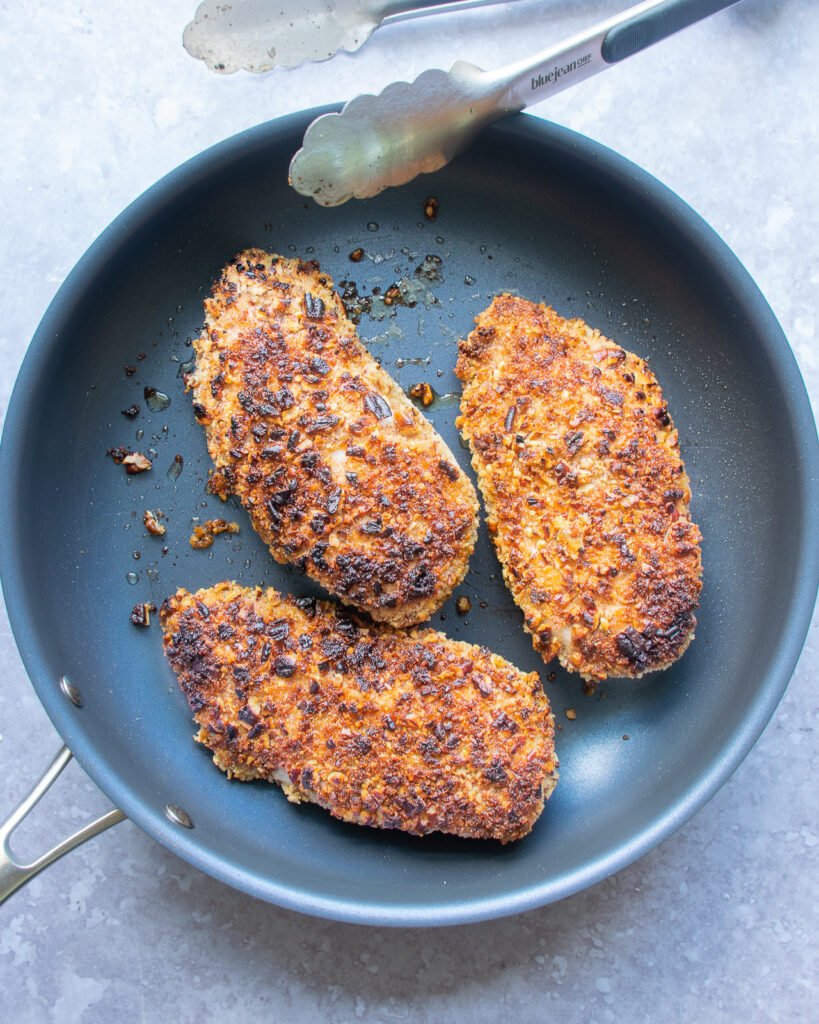 Chicken breasts cooking in a skillet.