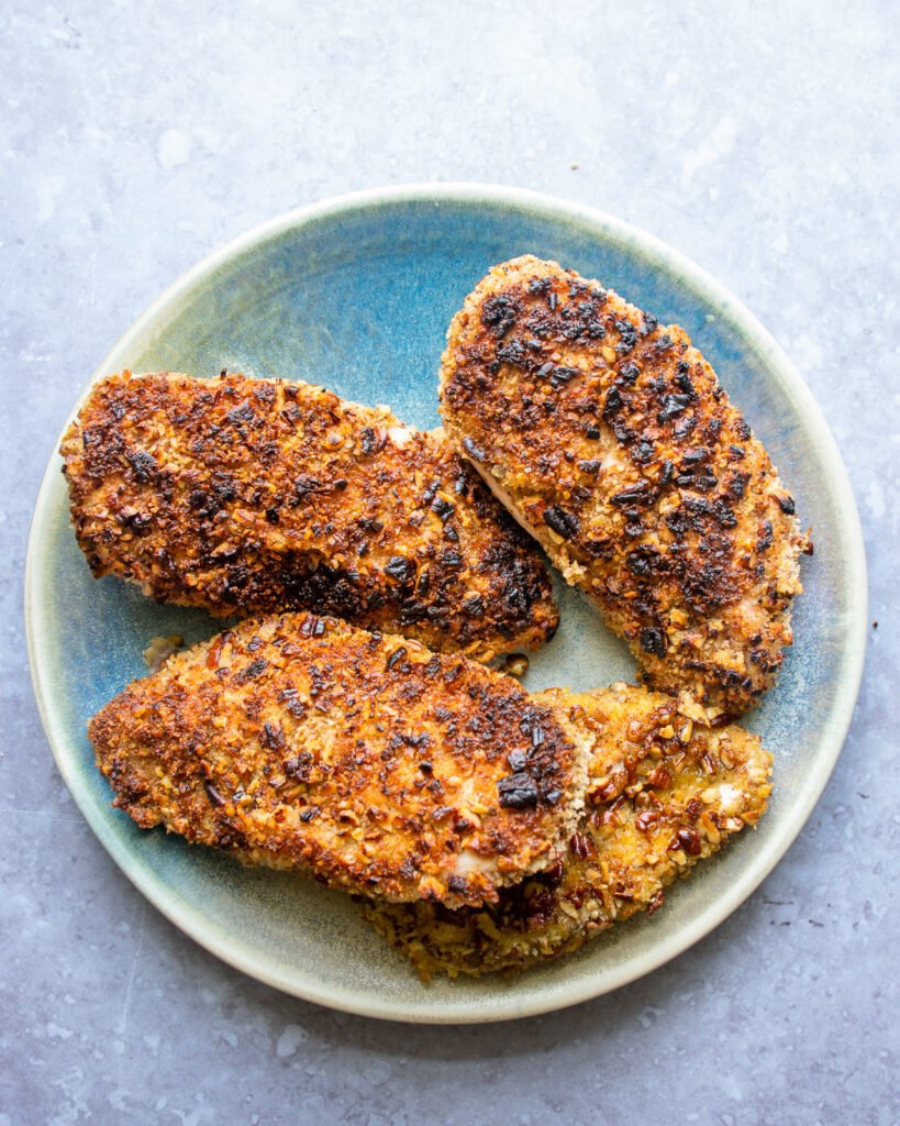 Coated chicken breasts on a blue plate on a countertop.