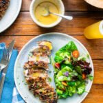 Pecan crusted chicken breast, sliced and fanned on a white plate with green salad and a honey mustard sauce.