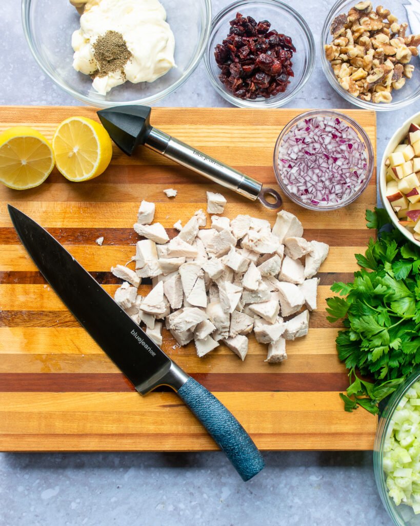 Looking down on a cutting board with a chef's knife and cut up chicken, with other ingredients.