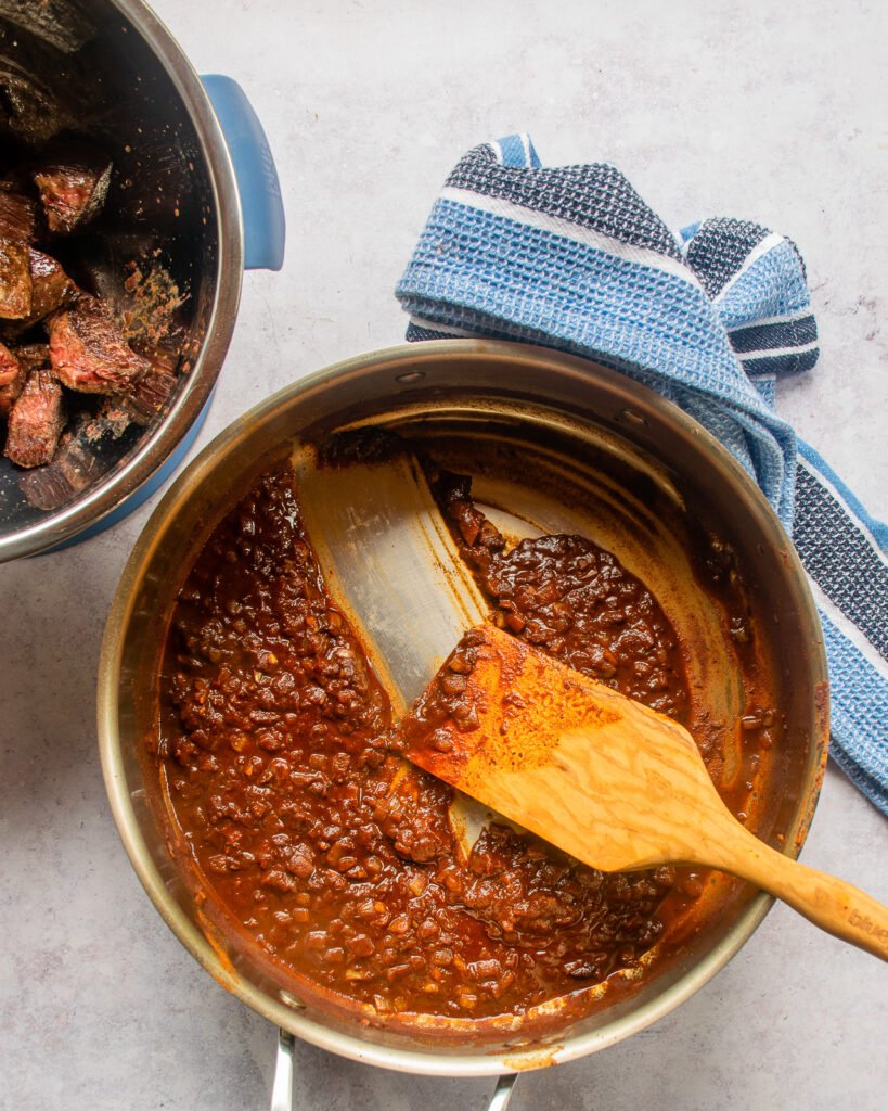 Sauce in a stainless steel sauté pan with a wooden spoon scraping along the bottom.