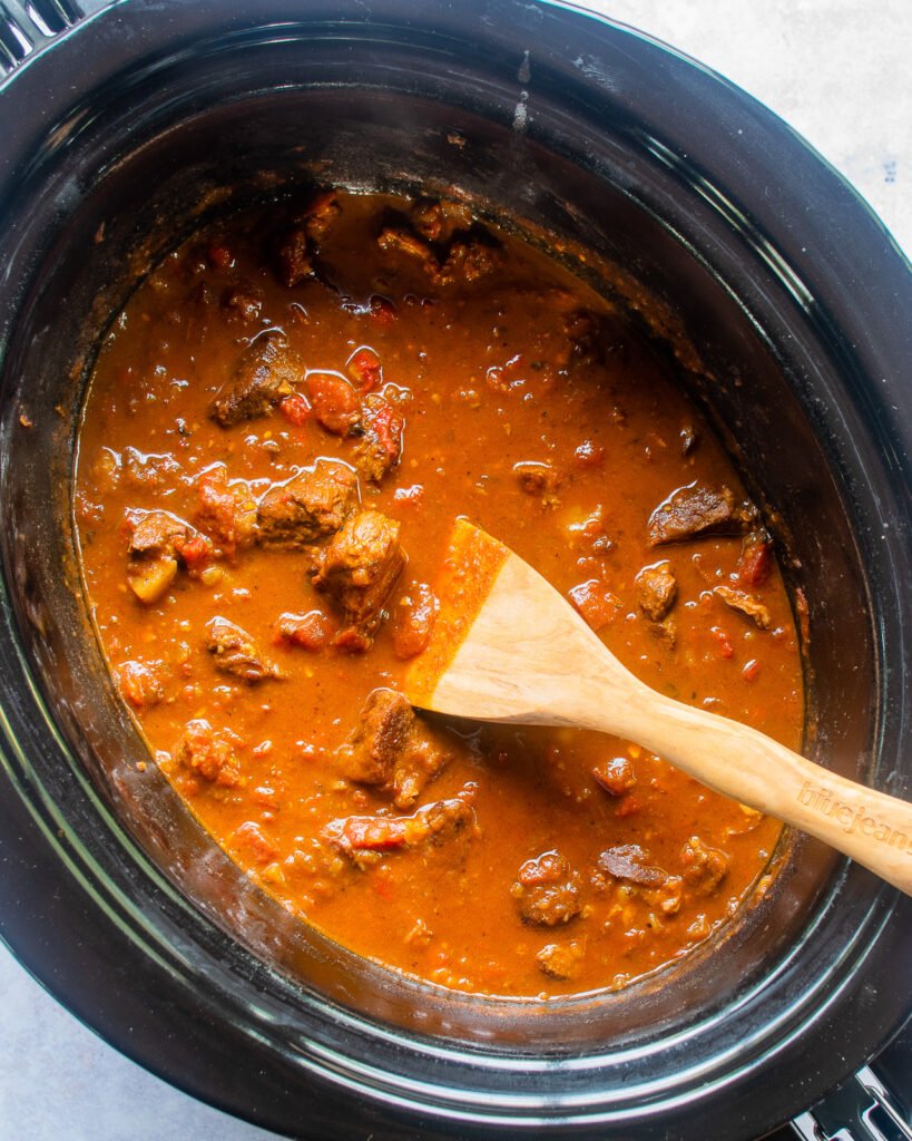 Finished Hungarian Goulash in a slow cooker with a wooden spoon sticking out of it.