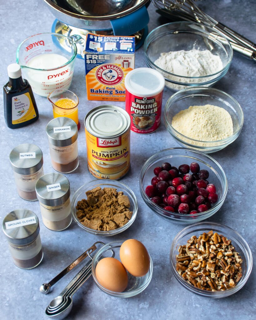 Ingredients on a countertop - pecans, cranberries, flours, eggs, sugar, spices, milk and a can of pumpkin.