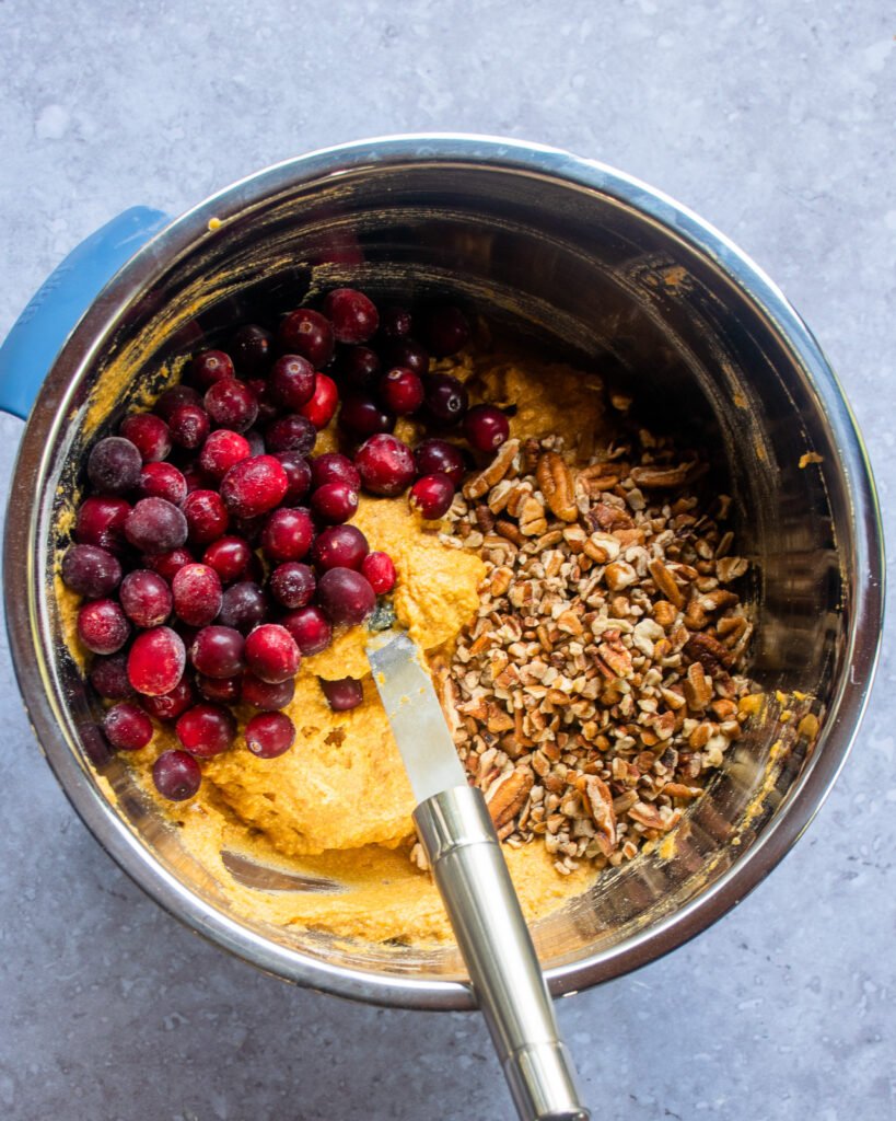 Looking down into a bowl with orange batter, fresh cranberries and pecans.