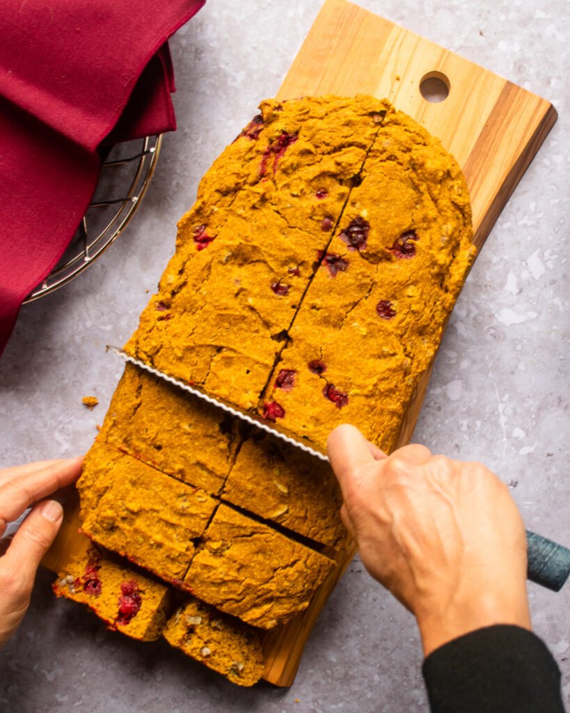 A hand cutting pumpkin cornbread into squares.