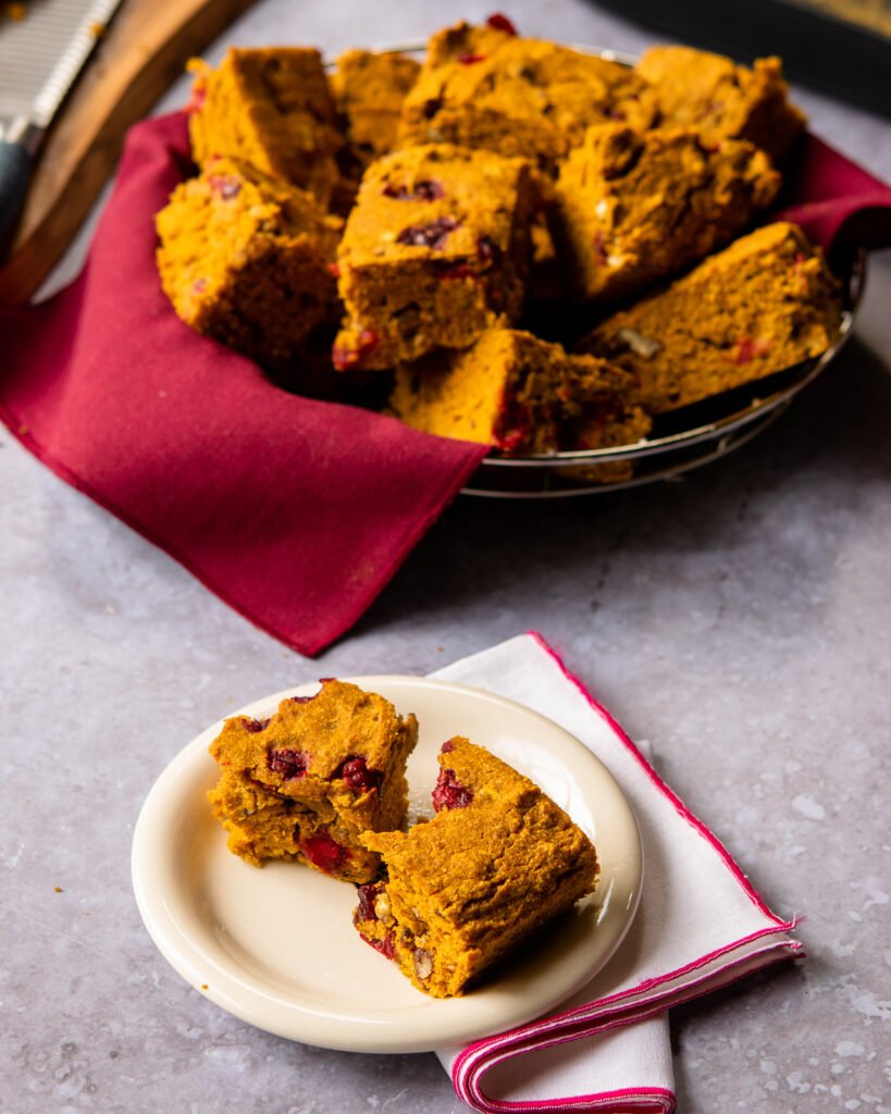 A piece of pumpkin cornbread on a white plate with a basket of cornbread in the background.