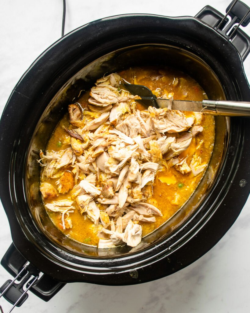 Shredded chicken added to a slow cooker of vegetables and liquid.