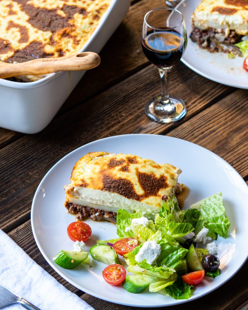 A dinner plate of moussaka with Greek salad on a table.