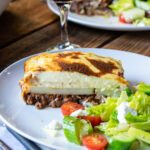 Close up of moussaka on a white plate with Greek salad.