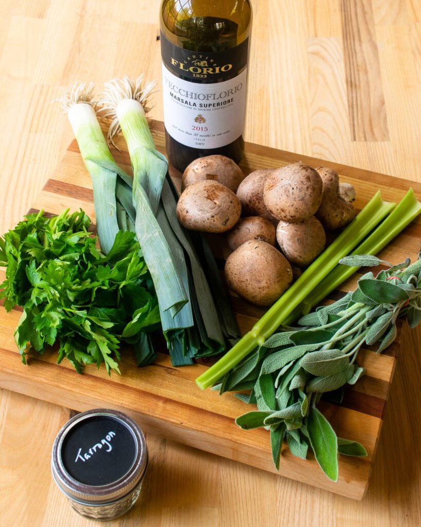 Ingredients on a cutting board - leeks, mushrooms, celery, sage, parsley, marsala wine and a jar of tarragon.