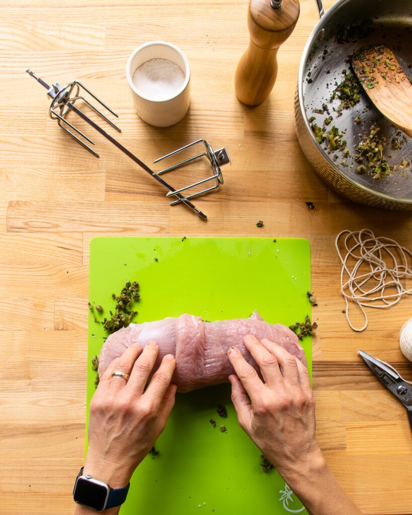 Hands finishing rolling up a double-butterflied turkey breast with a filling inside.