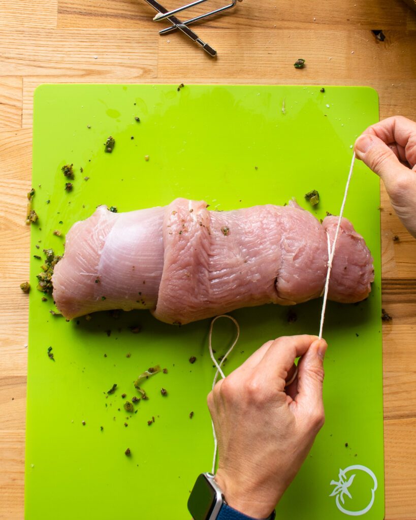 Hands tying the first loop around a turkey breast.