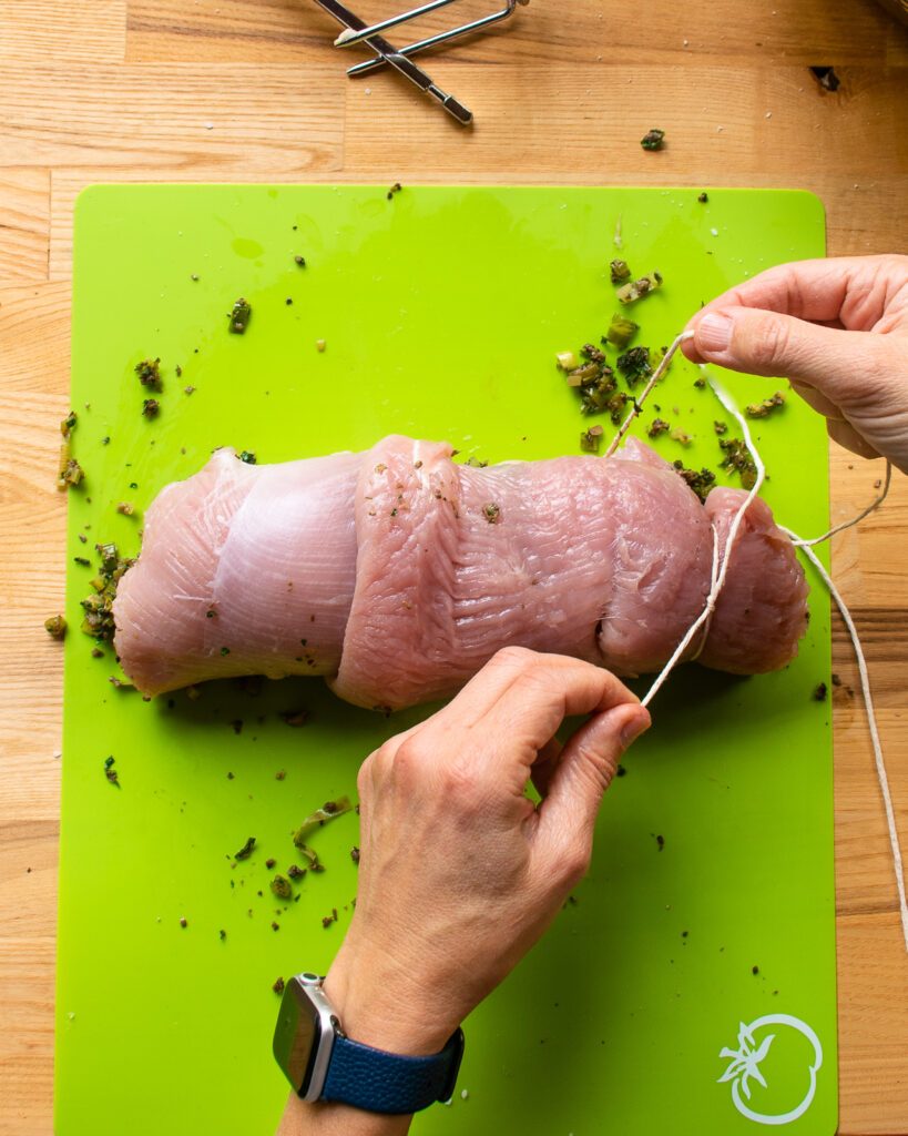 Hands starting to tie up a turkey roulade with kitchen twine.