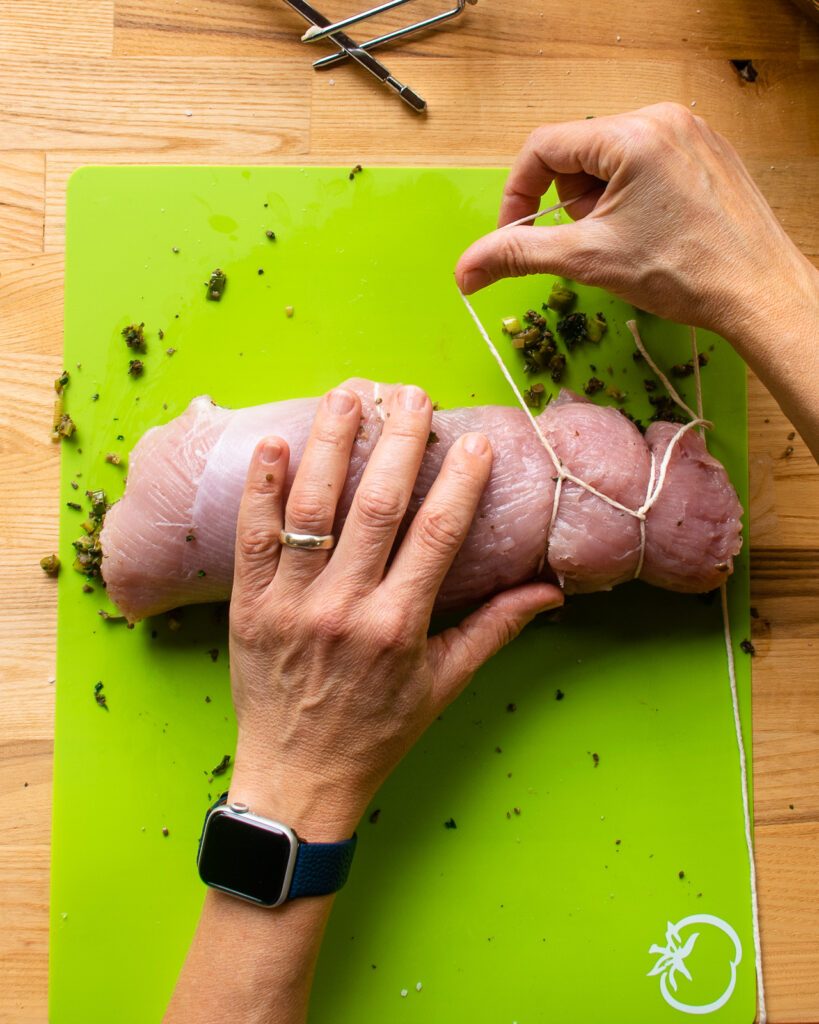 Hands tying a turkey roulade with kitchen twine.