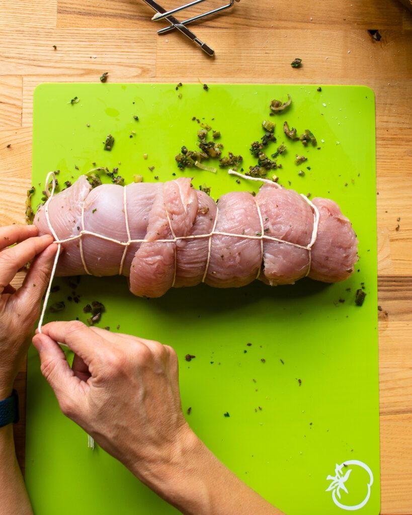 Two hands showing how to tie up a roast turkey breast.