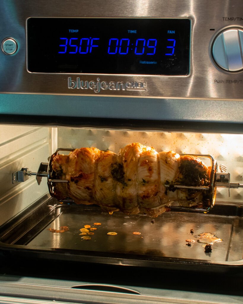 Turkey Roulade cooking in an air fryer oven on a rotisserie spit.