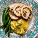 Close up straight down look at a china dinner plate of turkey roulade, gravy, green beans and mashed potato.