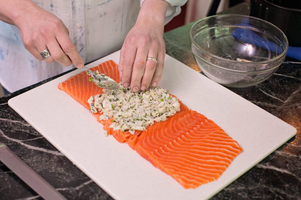 Hands placing a filling in a butterflied fillet of salmon.