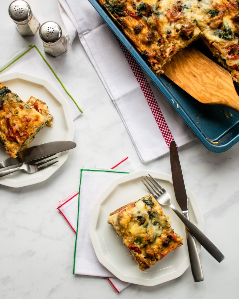 Looking down on two plates of breakfast strata with a large casserole of strata nearby.