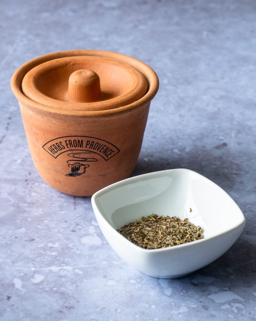 Herbs de Provence in a small terracotta pot and some herbs in a white dish.