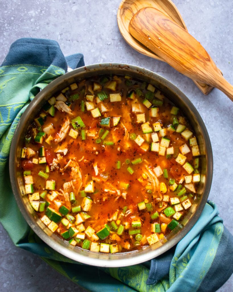 Looking straight down into a stockpot with chicken vegetable soup in it and a wooden spoon on a spoon rest beside it.