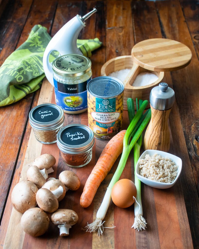 Ingredients on a wooden table - mushrooms, carrot, scallions, egg, breadcrumbs, spices, chickpeas, tahini.