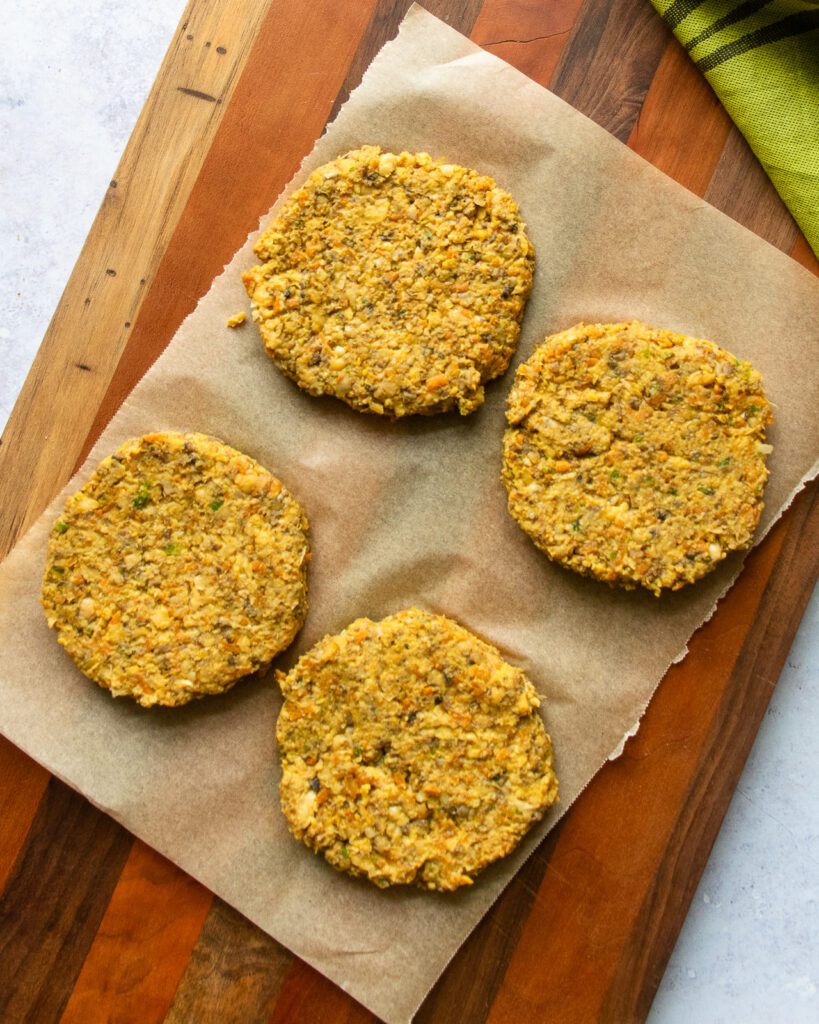 4 chickpea burger patties on parchment paper on a wooden cutting board.