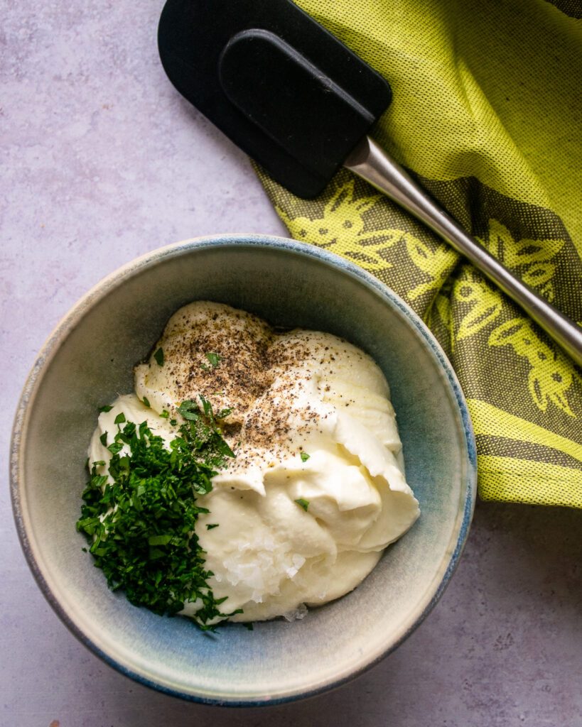 Whipped feta spread in a bowl with chopped parsley and ground pepper on top.