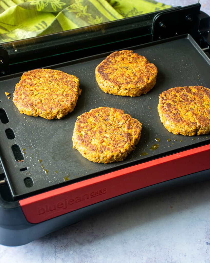 Chickpea burgers cooking on an electric griddle.