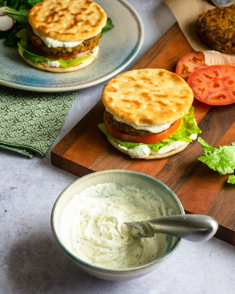 A small bowl of whipped feta spread with chickpea burgers in the background.