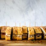 Mini muffaletta sandwiches on a cutting board with toothpicks in each sandwich.