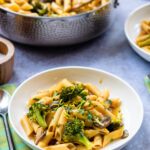 One pot pasta with mushrooms, leeks and broccoli in a white bowl with a stainless steel sauteuse with more on the table.