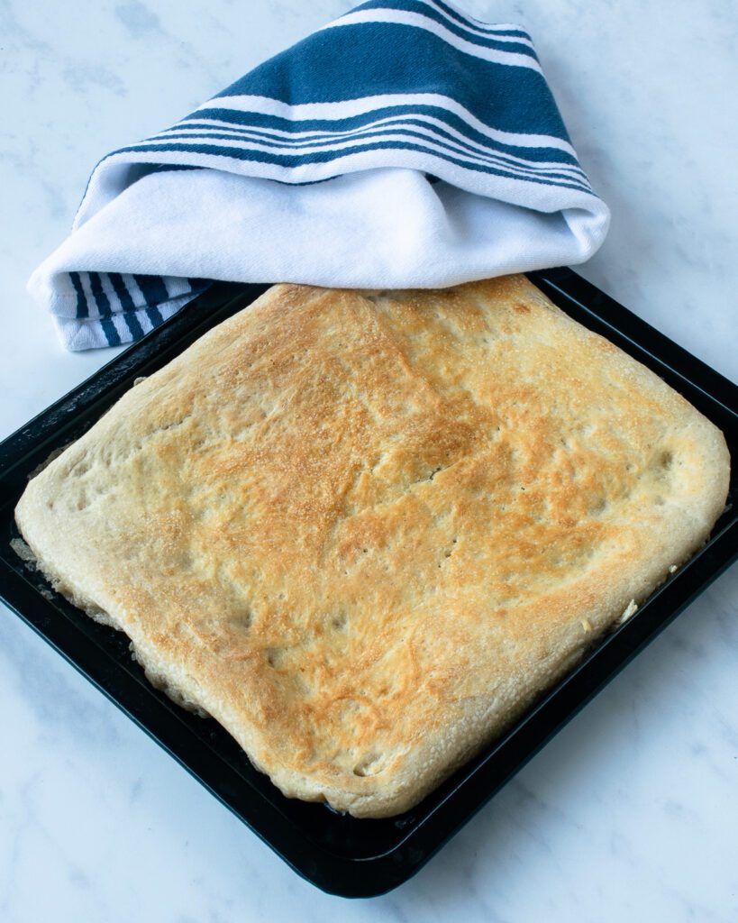 Par-baked pizza dough on a baking tray with a blue and white striped towel.