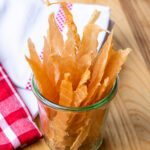 Chicken jerky strips sticking out of a glass jar with a red and white checkered napkin near by.