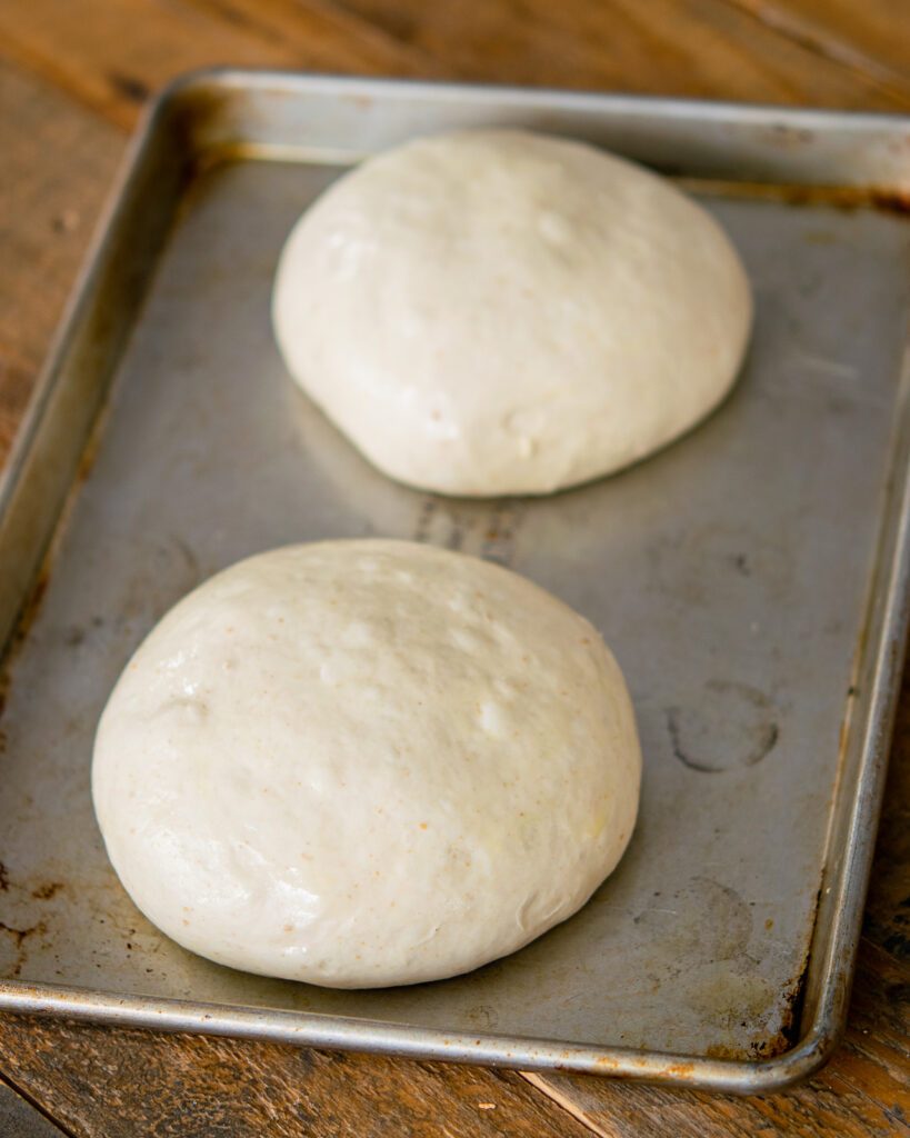 Two balls of dough on a baking sheet on a wooden table.