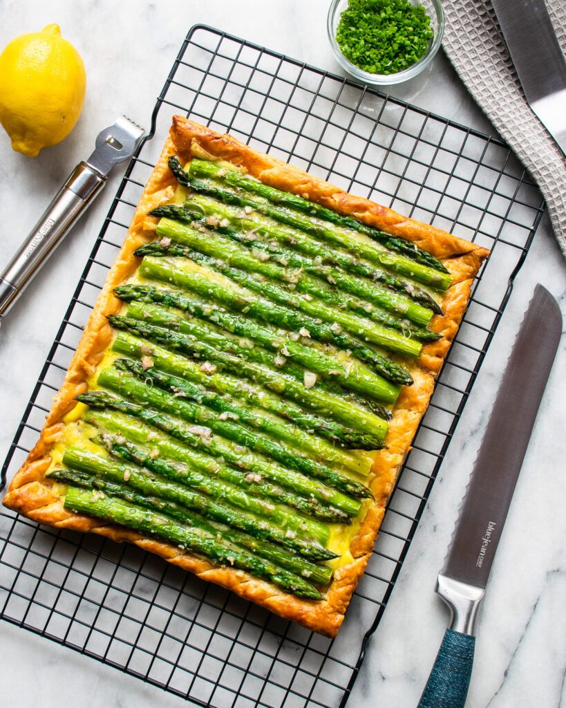 Baked Asparagus Tart on a cooling rack with  utensils and a lemon nearby.