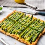 An asparagus tart on a piece of marble with kitchen tools around it.