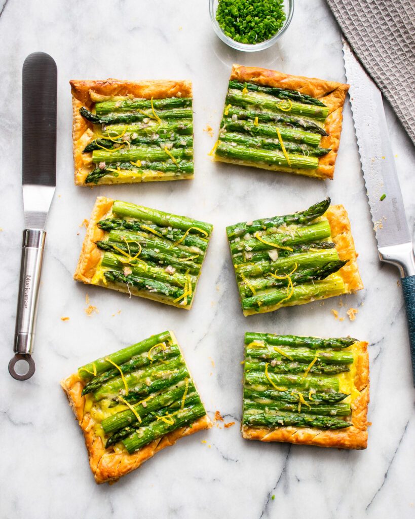Looking straight down at asparagus tart cut into 6 pieces on a marble board.