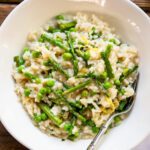 A white bowl with risotto with asparagus and peas on a wooden table.